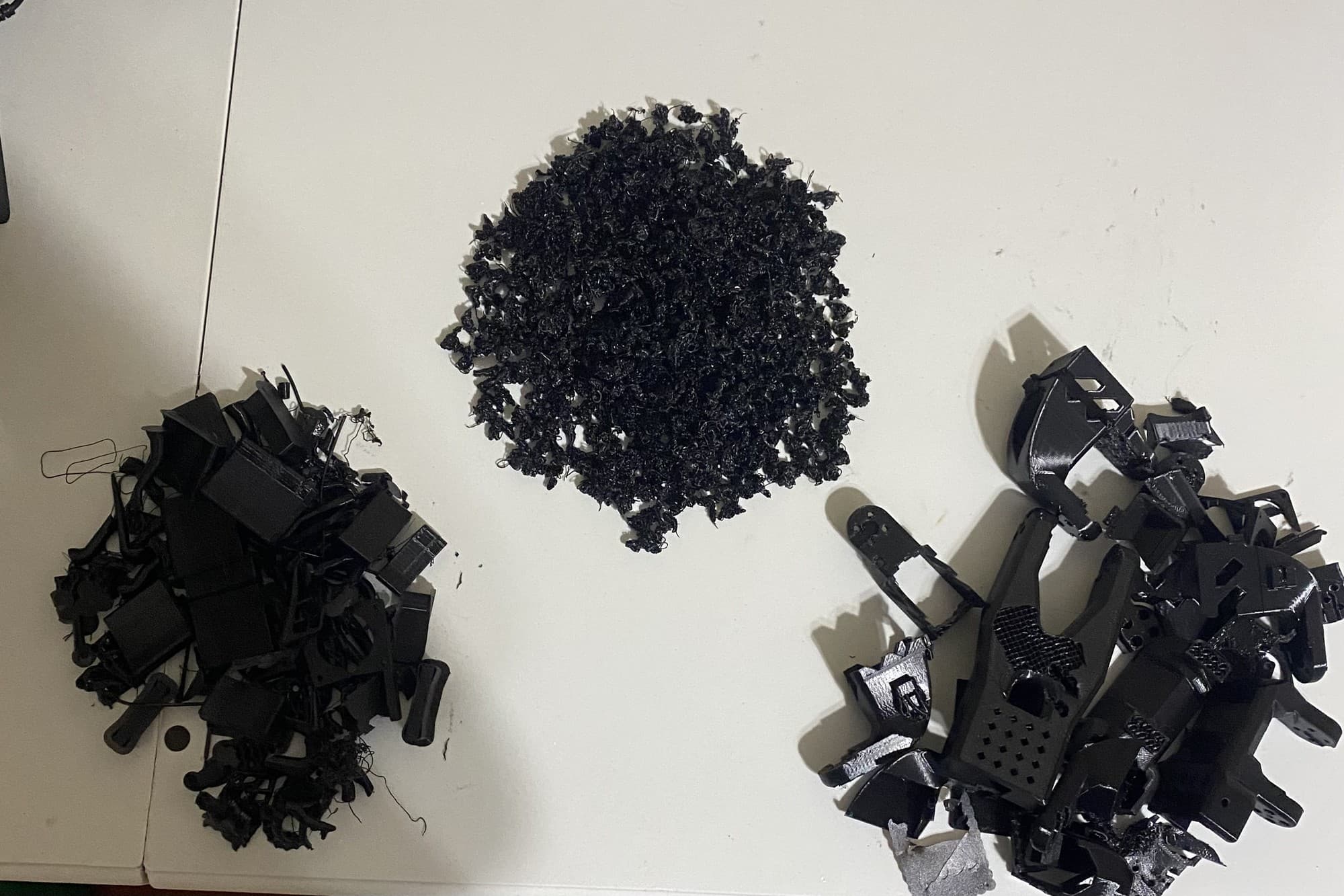 Filament waste and failed black 3D-printed robotic arm parts arranged on a table